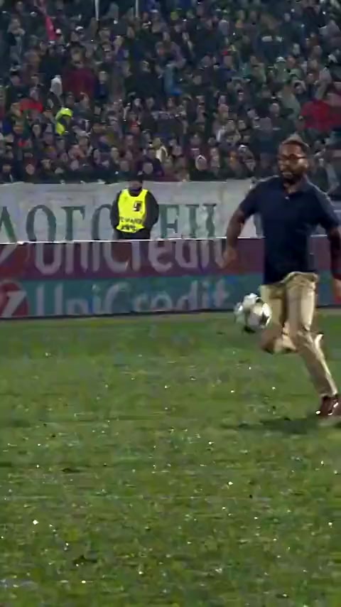 Sample Ozil Goal AI still: an adult man in a navy polo and khaki pants on a night pitch. Everyday clothes, not an athlete.